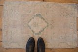 Distressed Oushak rug mat: beige and seafoam stepped geometric pattern with black boots.