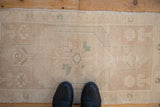 Distressed vintage Oushak rug edge in beige with soft green motif and worn pile.