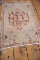 Distressed Oushak rug detail: beige field, dusty copper tendrils, and a zigzag border design.