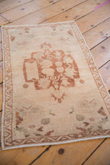 Distressed Oushak rug corner with softened beige pile and dusty copper geometric border.