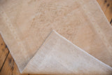 Distressed vintage Oushak rug corner, revealing worn beige pile and woven foundation with intact selvage.