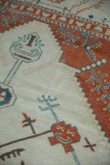 Serrated terracotta border alongside blue geometric plant motifs on a worn ivory Oushak pile.