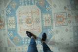 Time-softened sky blue and terracotta motifs on the worn, low pile of a vintage Oushak carpet.