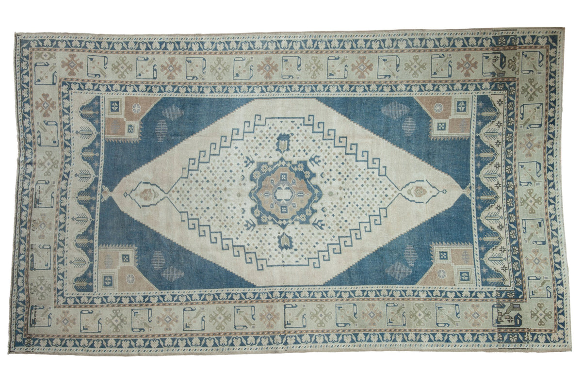Distressed vintage Oushak carpet with a geometric shadow medallion in dusty denim blue, ivory, and pale coffee brown.
