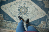 Low-pile texture of a distressed Oushak rug's dusty blue and ivory medallion.