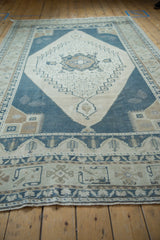 Low-angle view of a distressed Oushak carpet's geometric boteh border and soft, worn pile.