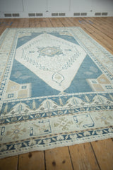 Perspective view of a distressed Oushak rug's geometric patterns in time-softened dusty blue and ivory tones.