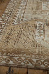 Distressed Oushak rug with muted ivory, sand, and brown ram's horn and scroll motifs.
