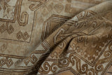 Folded vintage distressed Oushak rug showing worn pile and curvilinear patterns in brown and ivory tones.