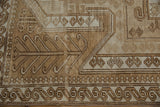 Distressed Oushak rug section with curvilinear ram's horn and geometric motifs in brown and beige.