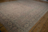 Distressed Oushak rug corner with patterned border and faded pink field.