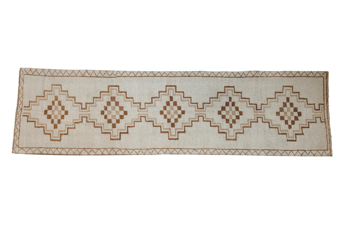 Distressed vintage Kars rug runner with interconnected stepped medallions in neutral coffee brown and beige tones.