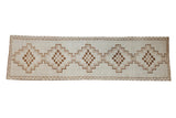 Distressed vintage Kars rug runner with interconnected stepped medallions in neutral coffee brown and beige tones.