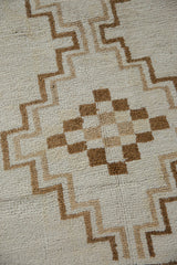 Close view of a checkered geometric medallion and stepped lines in brown and sand tones on a short, even pile.
