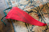 Red felt pennant showing dark green tie, white stitching, and surface discoloration.