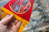 Vintage red felt flag close-up with blue roadway graphic, yellow trim, age marks.