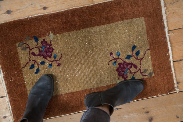 Overhead view of a vintage Nichols Art Deco rug mat for scale, showing floral details and a copper border, measuring 1'6
