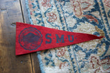 Angled close-up of vintage red felt SMU pennant with black school crest and letters.