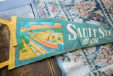 Detail of the boat graphic and yellow ties on a vintage Sault Ste Marie felt pennant.