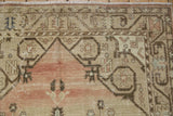 Distressed Oushak rug corner, showing abrashed pale blush field and beige stylized border.