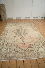 Angled view of distressed vintage Oushak rug with abrashed pale blush and tree of life motifs.