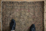Antique Persian Kerman rug field displays extensive wear, faded floral motifs, and threadbare spots.