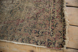 Visible foundation and worn fringe on an antique Kerman rug, displaying muted floral designs.