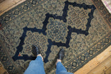 Antique Senneh rug with intricate Herati motifs, scalloped navy medallion, and aged ivory pile.