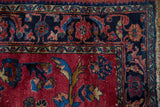 Corner of a 1940s vintage Persian Lilihan rug, cherry red field, navy blue floral border, and fringe.