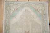 Distressed Oushak rug corner with worn pile, seafoam green stepped spandrel, and vined border.
