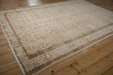 Distressed cream Oushak rug corner with brown floral patterns and pale blue accents, showing wear.