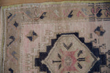Distressed Oushak rug corner, showing intact green-gold selvage and worn beige pile.
