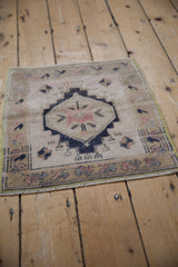 Distressed Oushak rug with decorative wear, beige field, dark navy stepped medallion, and pale blush motifs.