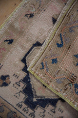Folded hand knotted Oushak rug shows distressed pile, dark motifs, woven back, and green selvage.