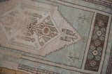 Close-up of geometric floral bouquet within the distressed Oushak rug's pale seafoam green spandrel.