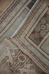 Folded vintage distressed Oushak rug showing pale seafoam and ivory geometric patterns.