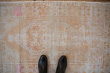 Distressed Oushak rug's low pile texture, revealing tangerine, fuchsia floral patterns on ivory.