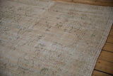 Distressed vintage Oushak carpet showing faded cream, sage vinery, and abrashes.
