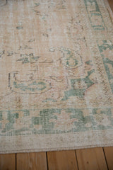 Distressed vintage Oushak rug corner, faded cream field, soft sage designs, and worn pile.