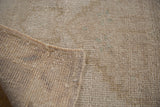 Vintage Oushak rug corner revealing reverse, intact side selvage, and distressed beige pile.