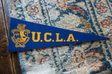 Gold school crest and blue felt texture on vintage UCLA pennant.
