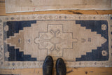 Distressed vintage Oushak mat runner with a stepped medallion, dusty navy blue and beige pile.