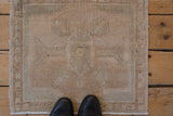 Distressed vintage Oushak mat in beige and pale seafoam, shown for scale.