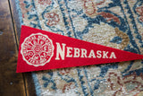 Circular off-white crest on a red felt vintage Nebraska University pennant.