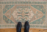 Vintage distressed Oushak runner showing abrashed field with pale turquoise and beige floral designs.