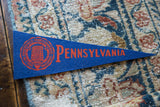 Royal blue felt Pennsylvania University pennant with red crest on a hand-knotted rug.
