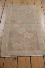 Vintage distressed Oushak rug mat viewed from a high angle, showing its soft sand and celadon floral pattern.