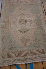 Distressed Oushak rug corner showing soft beige pile and a stepped celadon green border.