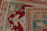 Oushak rug corner revealing short cherry red pile, fringe, and woven back with wave border.