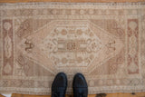 Distressed vintage Oushak rug, showcasing faded central floral medallion and stepped field, with shoes.